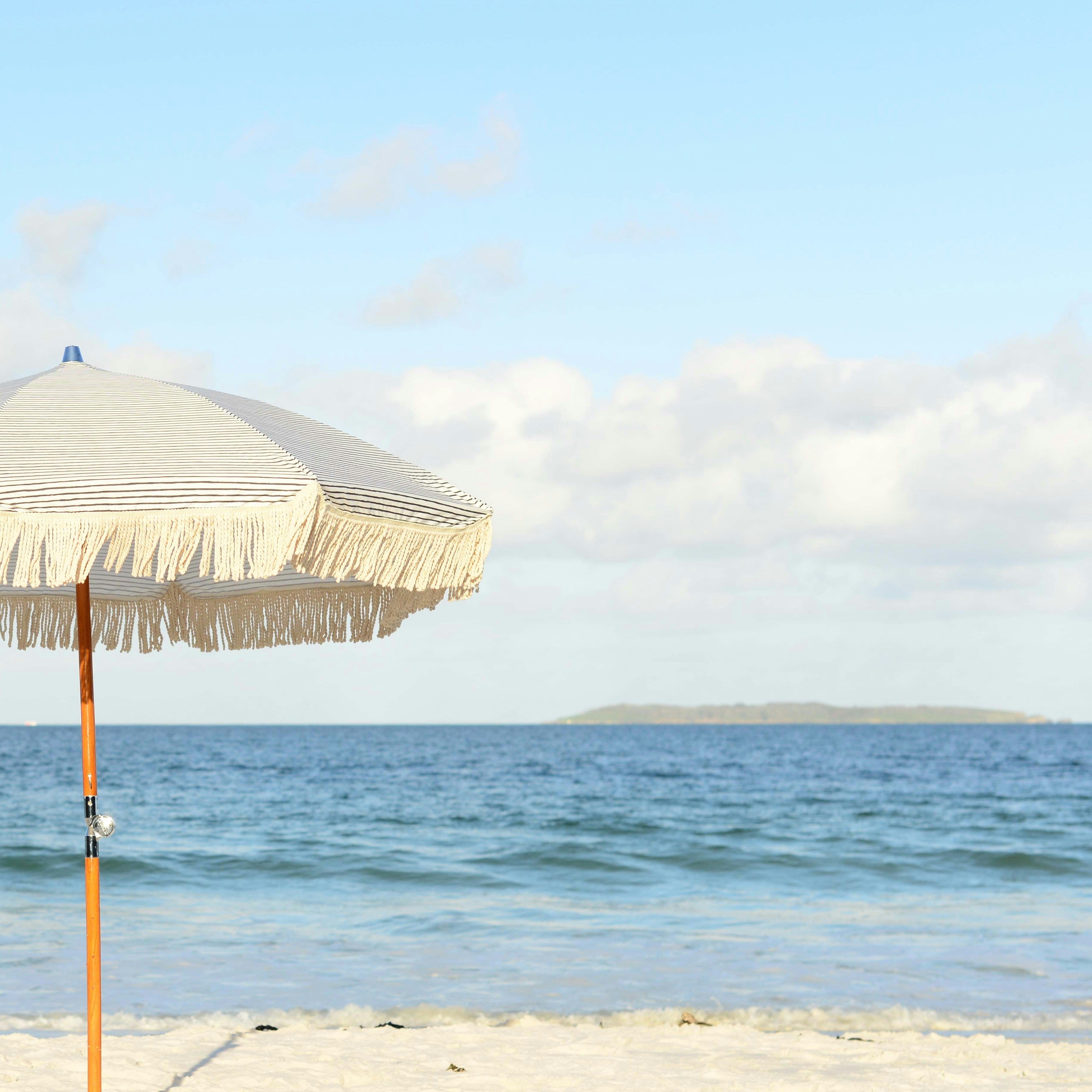 Parasol en tissu clair sur une plage face à la mer. Light-colored fabric parasol on a beach facing the sea.