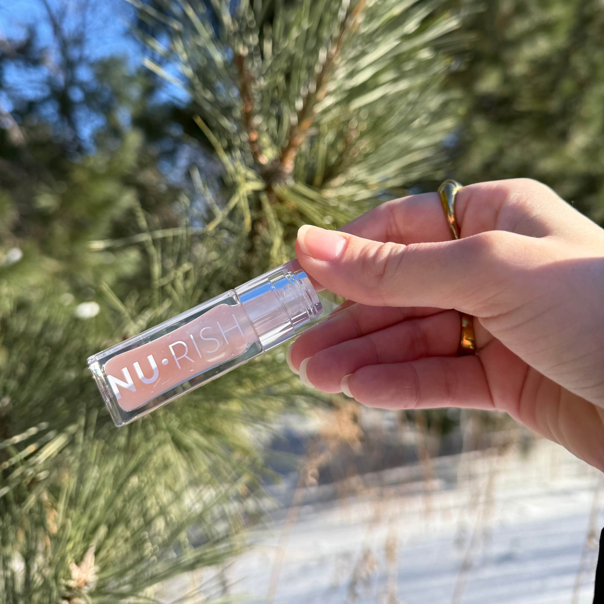 Lip Oil NURISH avec en fond de la neige et un sapin.