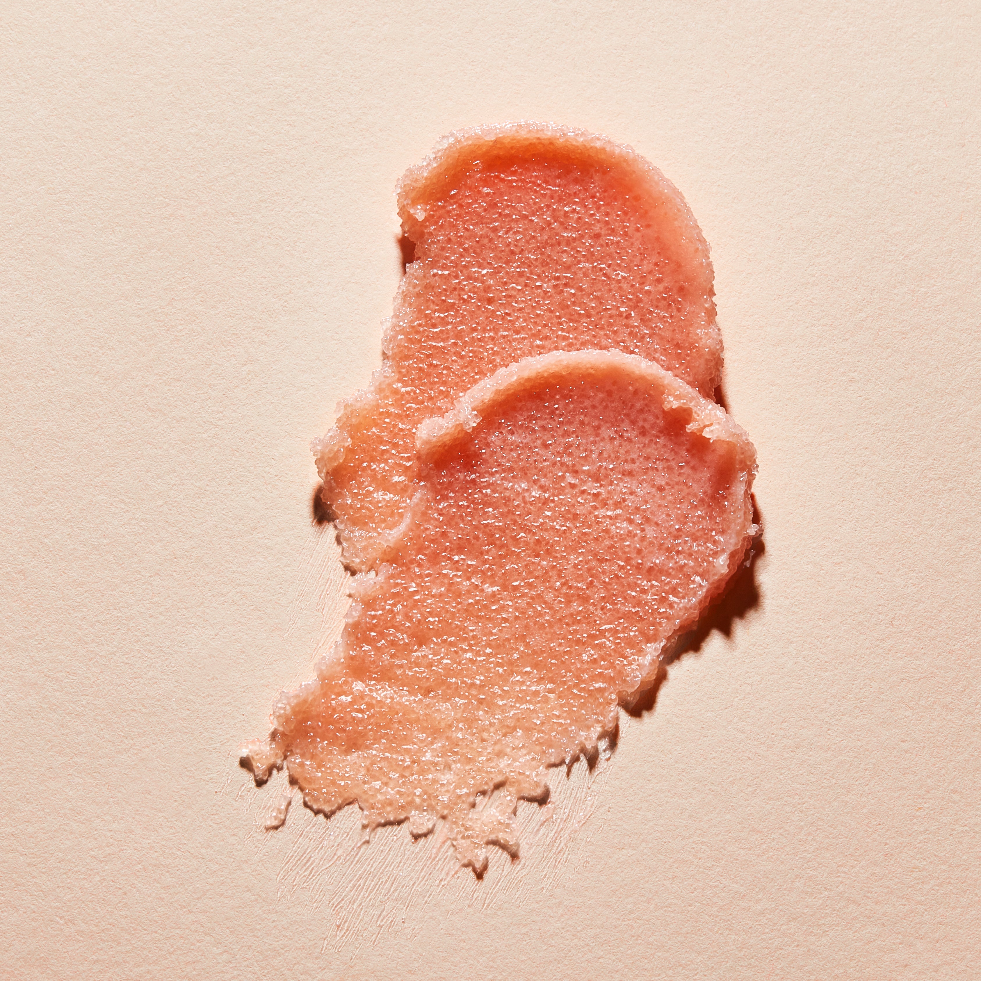 Texture de gommage lèvre NU•RISH étalée sur fond beige, exfoliant naturel à grains fins pour lisser es lèvres et éliminer les cellules mortes. NU•RISH lip scrub texture spread on a beige background, a natural exfoliant with fine grains to smooth lips and remove dead skin cells.